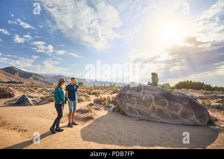 Couple in blue checkered shirt in the open air museum near stone with ancient petroglyph of goats at Kyrgyzstan. Culture Heritage Museum. Stock Photo