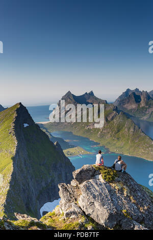 Two hikers rest after reaching the summit of Munkan, a classic hike in the Lofoten Islands. Stock Photo