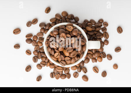 White china espresso cup viewed from above on white background with brown roasted coffee beans overflowing Stock Photo