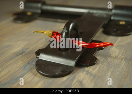 Old metal hasp and staple lock with a red hot chili pepper threaded through it in a conceptual image on a wood background Stock Photo