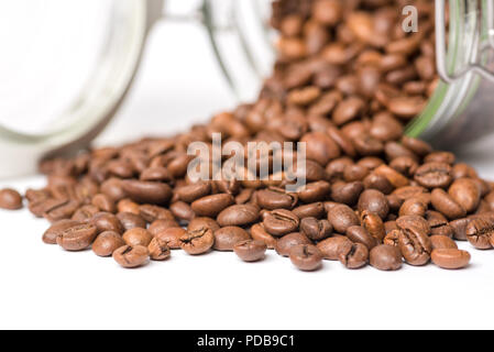 Glass food storage jar lying on side with coffee beans spilling out on white surface Stock Photo