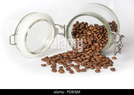 Glass food storage jar lying on side with coffee beans spilling out on white surface Stock Photo
