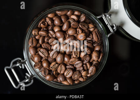 Roasted coffee beans in clip top storage jar viewed from above on black background Stock Photo