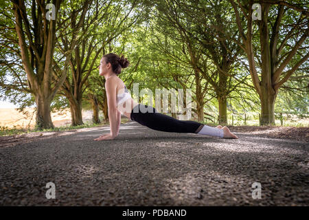 woman practicing yoga outside doing an upward facing dog pose. Stock Photo