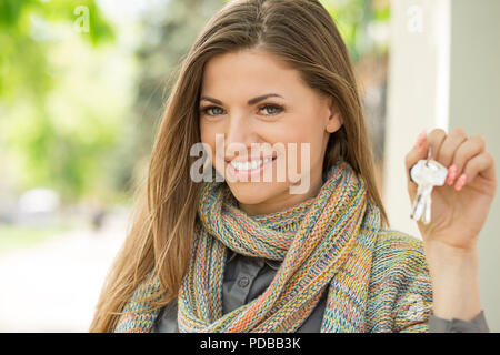 Happy pretty young woman showing key from new apartment smiling at camera and standing on street Stock Photo