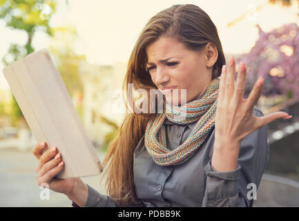 Young woman looking frustrated and grumpy being unhappy with tablet function having bad connection on street Stock Photo