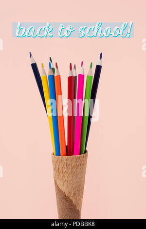 closeup of some pencil crayons of different colors in an ice cream cone and the text back to school on a pink background Stock Photo