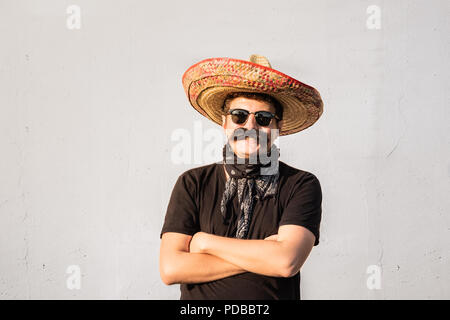 Funny and cheerful man dressed up in traditional mexican sombrero, false moustache, bandana and sunglasses. Movember or halloween concept of young mal Stock Photo