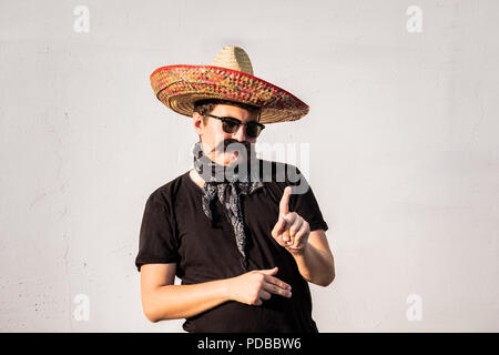 Funny and cheerful man dressed up in traditional mexican sombrero, false moustache, bandana and sunglasses. Humorous movember or halloween concept of  Stock Photo