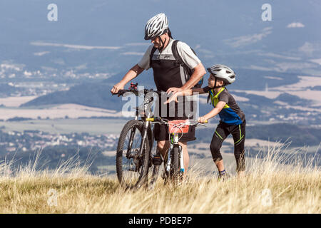 Bikers cycling on a mountain trail, Father and son, Velka Javorina mountain, Czech Slovak border in White Carpathians Man pushing Bicycle uphill Stock Photo