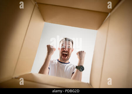 The surprised man unpacking, opening carton box and looking inside. The package, delivery, surprise, gift lifestyle concept. Human emotions and facial expressions concepts Stock Photo