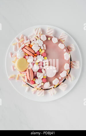 top view of pink birthday cake with marshmallows and macaroons on white plate Stock Photo