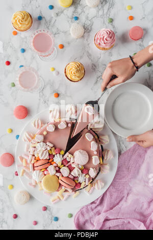 cropped view of woman putting piece of pink birthday cake with marshmallows on plate Stock Photo