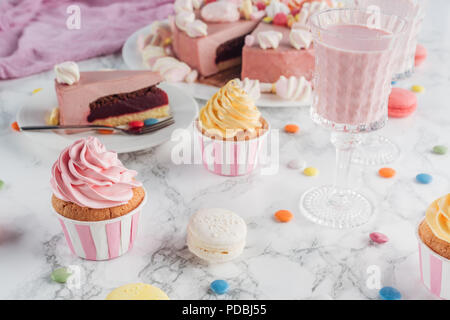 close up of pink cake, marshmallows, candies, sweet cupcakes and milkshake on marble table Stock Photo