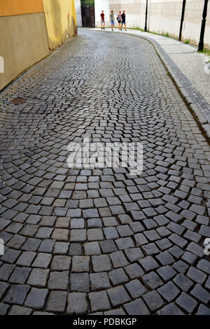 View down old narrow cobblestone paved road between buildings with pedestrians walking at end Stock Photo