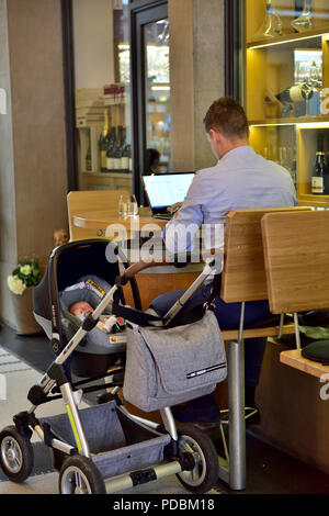 Man working on a computer laptop in public cafe with child in pram next to him Stock Photo