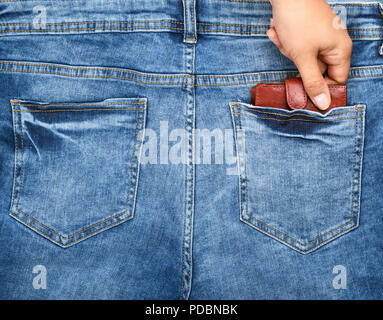 human hand pulls out of the back pocket of blue jeans a brown leather purse, the concept of stealing Stock Photo