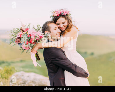 The outdoor portrait of the cheerful newlyweds. Groom is carrying the bride in the mountains. Stock Photo