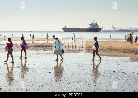 Holidaymakers walk along the beach, the Plage du Butin, at Honfleur as an oil tanker passes out to sea down the Seine Estuary by Le Havre Stock Photo