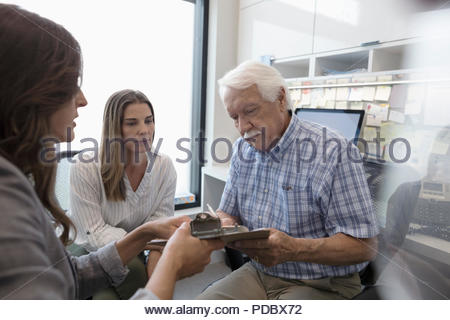 Female doctor guiding senior male patient with daughter signing paperwork in clinic office