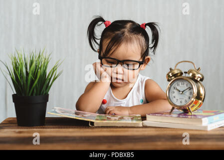 cute serious looking little asian toddler wearing spectacle reading a book on a table. concept of education, child development, growth and eye care Stock Photo