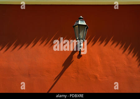 Street lamp on a painted red wall with long shadows in the old town Stock Photo