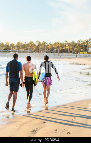 Male surfers walking with surfboards on sunny ocean beach Stock Photo