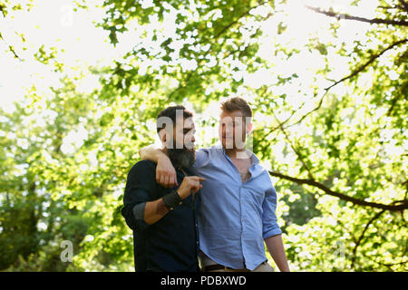 Affectionate male gay couple walking in sunny park Stock Photo