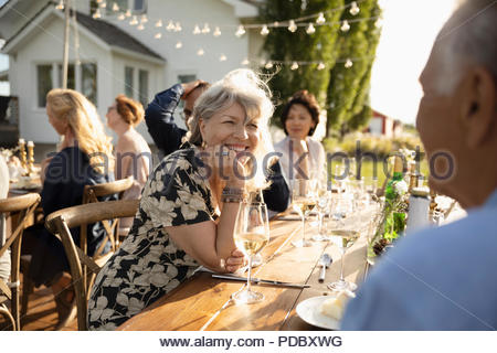 Smiling woman drinking wine, talking with man at sunny garden party