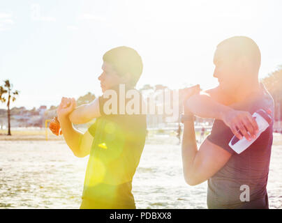 Male runners stretching arms on sunny beach Stock Photo