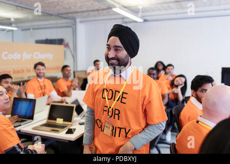 Happy, confident hacker in turban coding for charity at hackathon Stock Photo