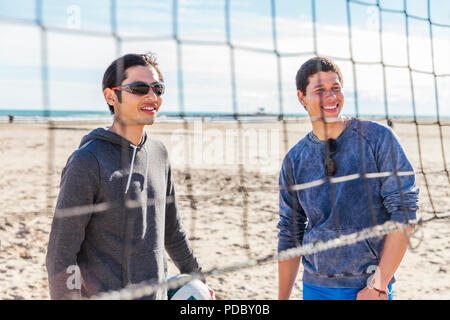 Smiling men playing beach volleyball on sunny beach Stock Photo