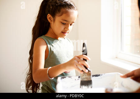 Girl painting, dipping paintbrush in tray Stock Photo