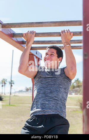 Determined man doing pull-ups on monkey bars Stock Photo