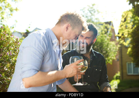 Happy male gay couple drinking wine in sunny garden Stock Photo