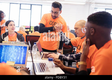Hackers handshaking, celebrating and coding for charity at hackathon Stock Photo