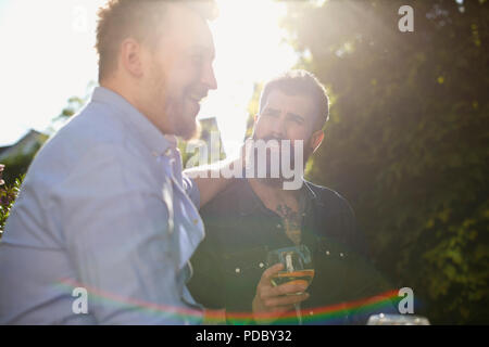 Affectionate male gay couple drinking wine in sunny garden Stock Photo