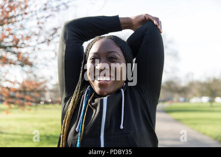 Portrait confident female runner stretching arms in park Stock Photo