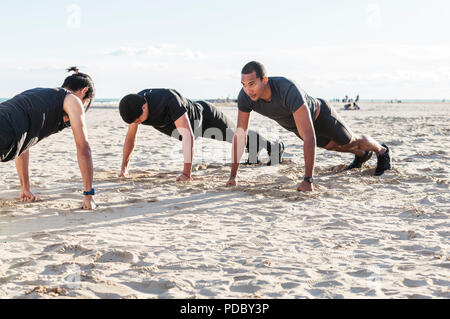 Men doing push-ups on sunny beach Stock Photo