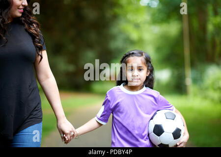 Portrait girl with soccer ball holding hands with mother Stock Photo