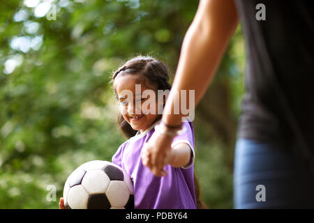 Smiling girl with soccer ball holding hands with mother Stock Photo