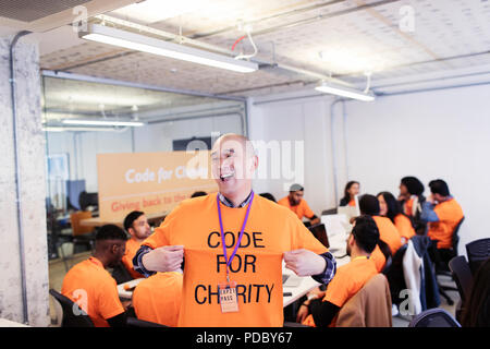 Playful hacker with t-shirt coding for charity at hackathon Stock Photo