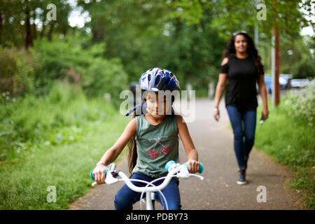 Mother watching daughter bike riding on path Stock Photo