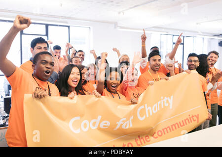 Portrait enthusiastic hackers cheering with banner, coding for charity at hackathon Stock Photo