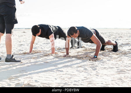 Men doing push-ups on sunny beach Stock Photo