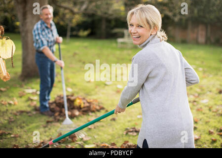 Portrait happy mature woman raking autumn leaves in backyard Stock Photo