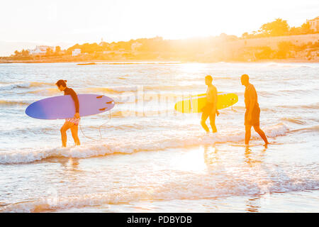 Male surfers carrying surfboards into ocean on sunny beach Stock Photo