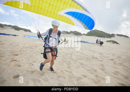 Female paraglider with parachute running, taking off on beach Stock Photo