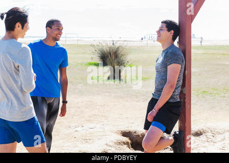 Male runners resting, talking in sunny park Stock Photo