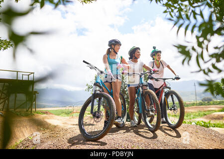 Women friends mountain biking on sunny obstacle course trail Stock Photo